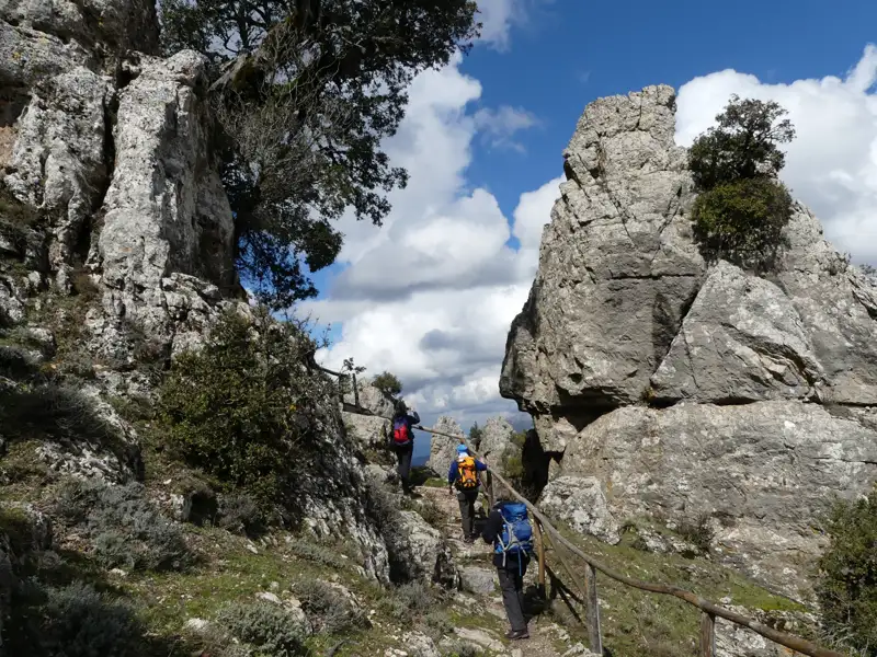 Wanderer auf einem Bergpfad mit Felsformationen und Geländer.