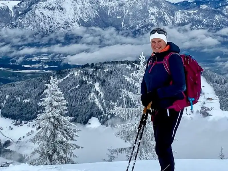 Wanderer mit Rucksack und Wanderstöcken auf einem schneebedeckten Berggipfel.