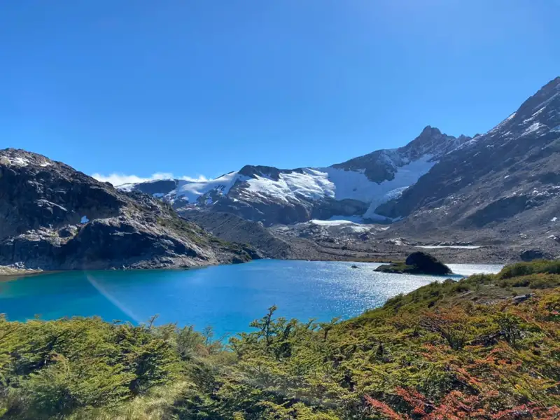 Türkisfarbener Bergsee mit schneebedeckten Bergen und Gletschern im Hintergrund.