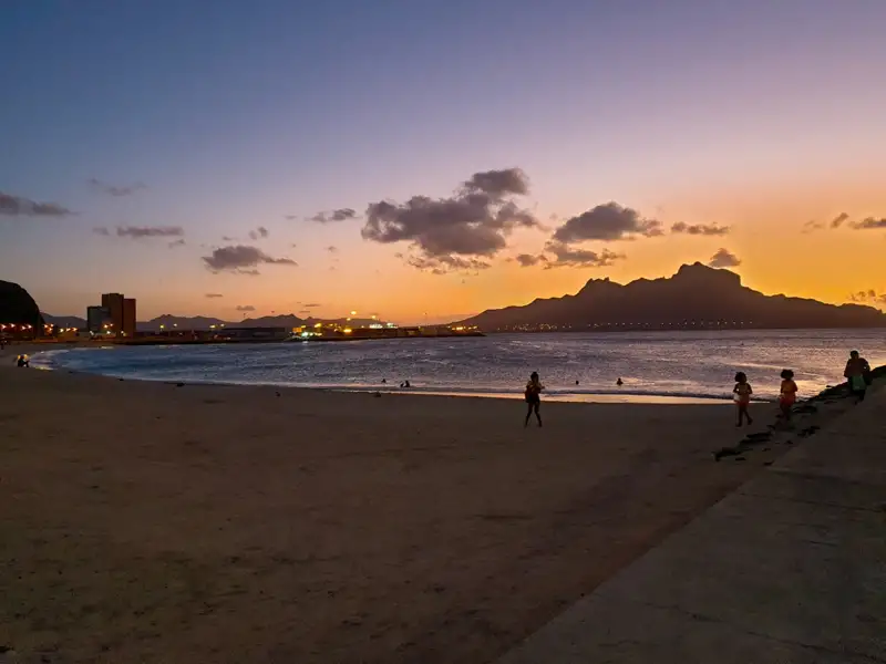 Sonnenuntergang über einem Strand mit Menschen, die am Ufer entlang gehen.