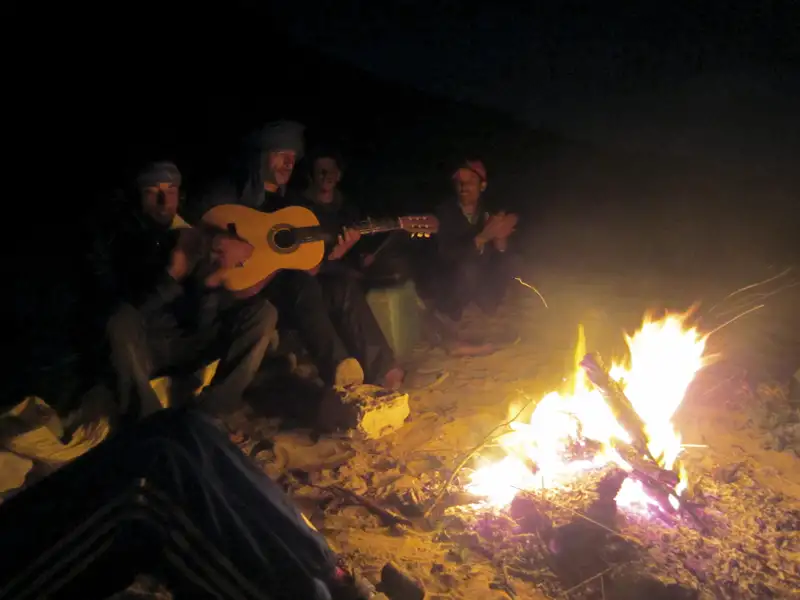 Reisende sitzen um ein Lagerfeuer und spielen Gitarre.
