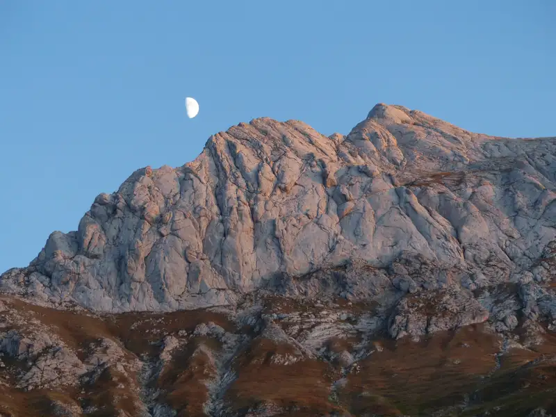 Felsige Berglandschaft im Abendlicht mit dem Mond am Himmel.