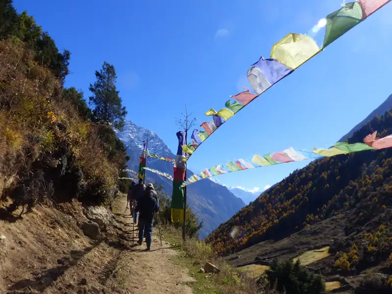 Wanderer auf einem Bergpfad mit bunten Gebetsfahnen und Blick auf die Berge.