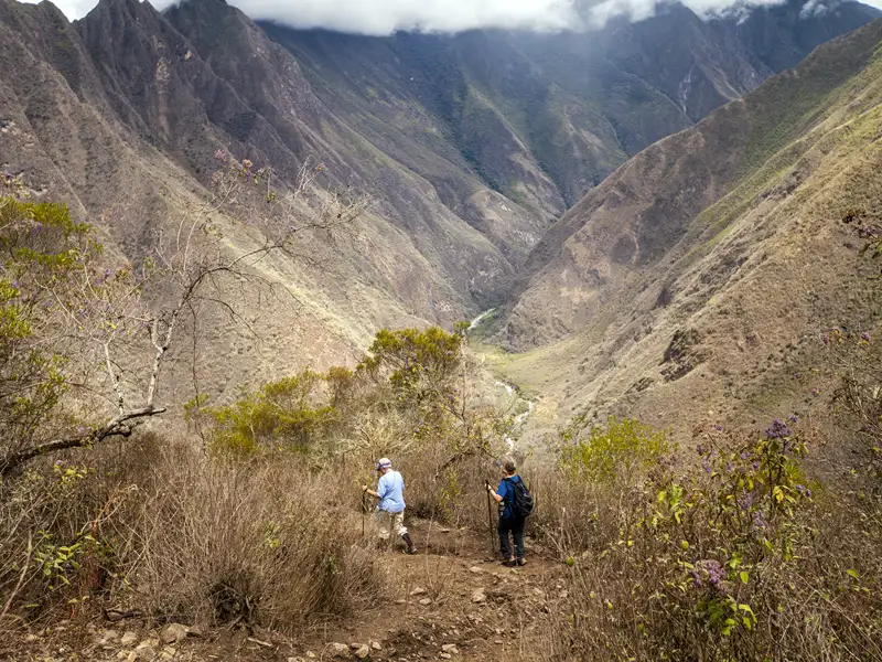 Zwei Wanderer auf einem Bergpfad mit Blick auf ein Tal.