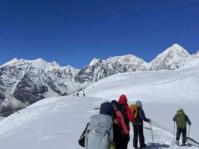 Wanderer mit Rucksäcken und Wanderstöcken in einer verschneiten Berglandschaft.