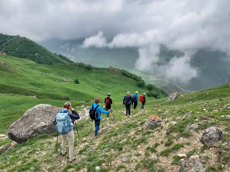 Wanderer auf einem Bergpfad mit Blick auf ein bewölktes Tal.