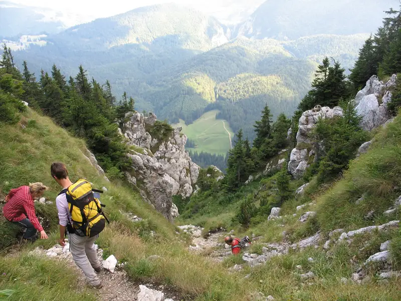 Wanderer auf einem steinigen Bergpfad. Im Hintergrund erstreckt sich ein Tal mit Wald und Wiesen.