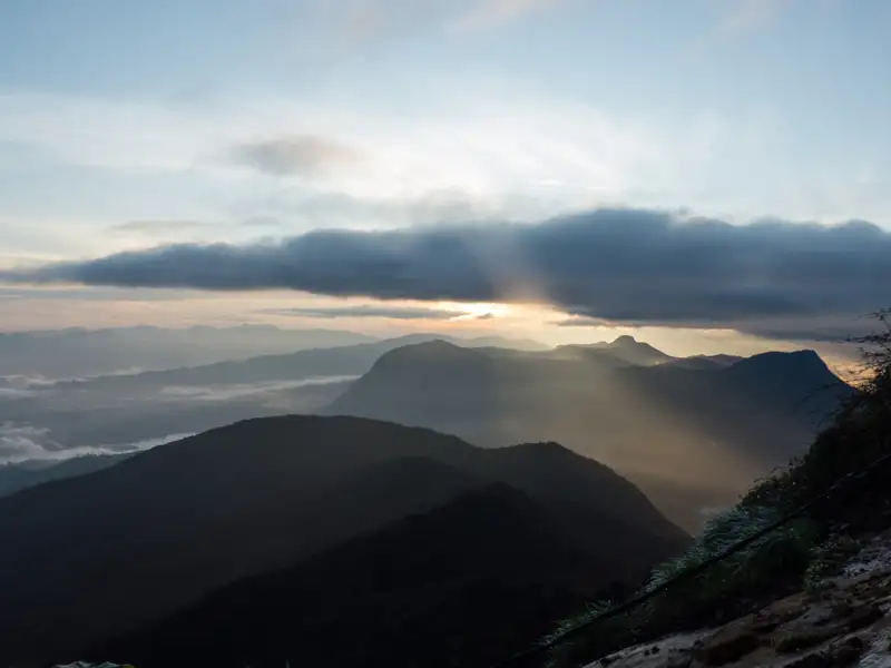 Sonnenstrahlen brechen durch die Wolken über einer Berglandschaft beim Sonnenaufgang.