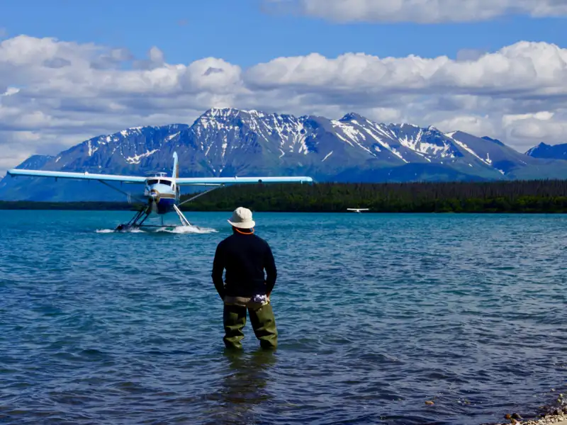 Wasserflugzeug landet auf einem See mit Bergen im Hintergrund.
