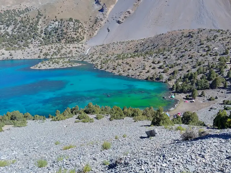 Türkisblauer Bergsee mit Zelten am Ufer und felsiger Umgebung.