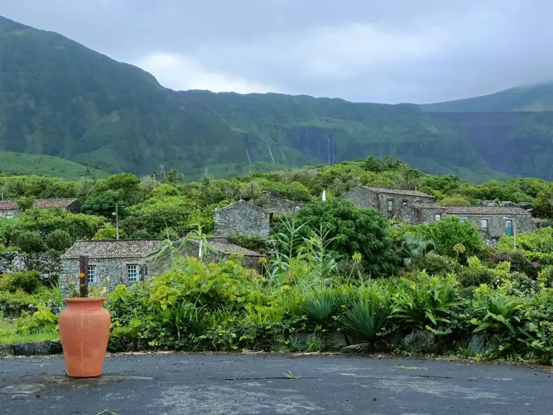 Traditionelles Steindorf mit üppiger Vegetation und bergigem Hintergrund.