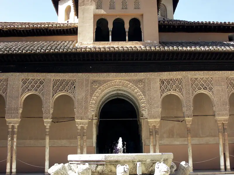 Maurische Architektur mit kunstvollen Bögen, Säulen und Ornamenten, zentriert um einen Brunnen.