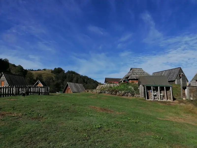 Rustikale Berghütten mit Holzzäunen und einer Berglandschaft im Hintergrund.