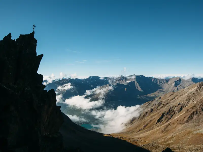 Panoramablick von einem Berggipfel mit Gipfelkreuz auf die umliegende Berglandschaft.