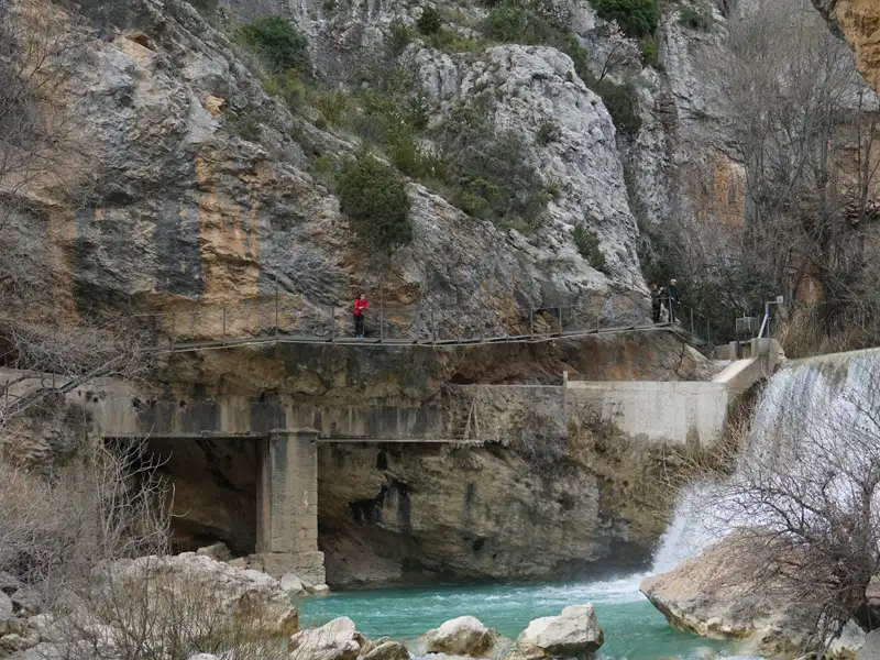 Wanderweg entlang einer Schlucht mit Wasserfall und türkisfarbenem Fluss.