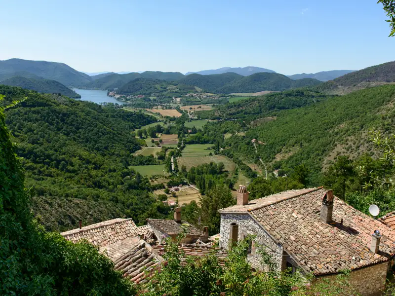 Panoramablick über ein Tal mit See und Häusern mit Ziegeldächern.