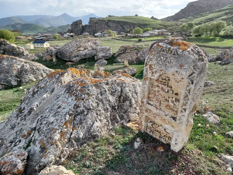 Alter Grabstein mit arabischer Schrift in felsiger Landschaft.