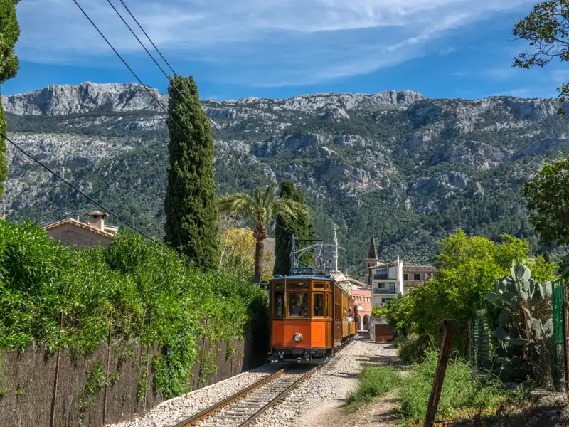 Historische Straßenbahn auf Schienenstrecke inmitten der Landschaft Mallorcas mit Bergen im Hintergrund.