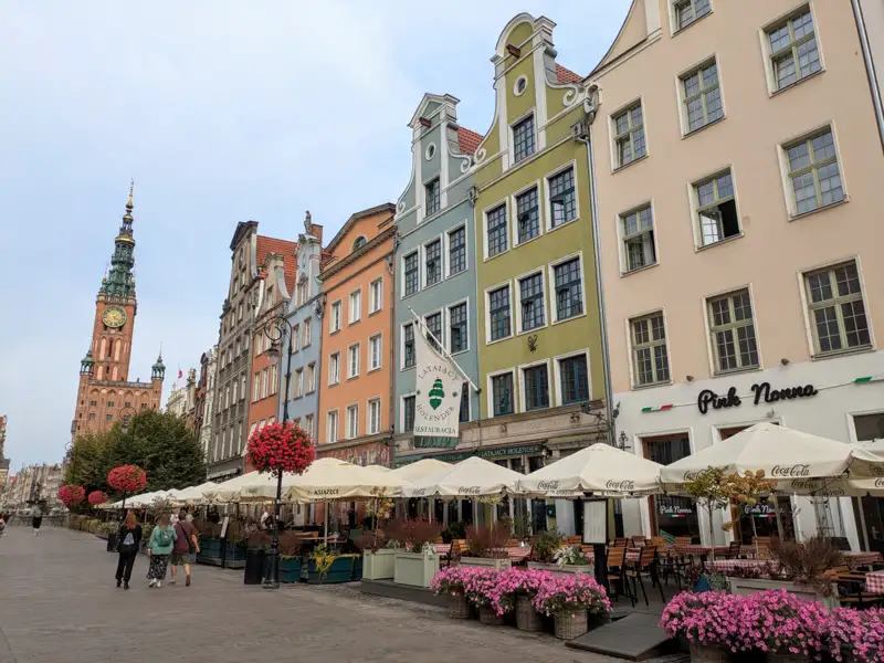 Blick entlang einer Straße mit bunten Häuserfassaden und Straßencafés in Richtung des Rathausturms.