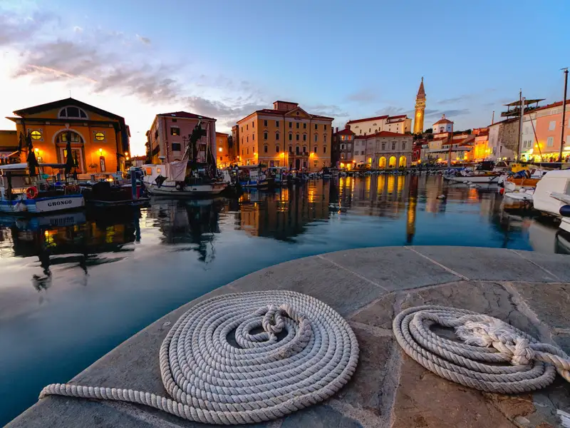 Abendliche Hafenansicht mit Booten und beleuchteten Gebäuden.