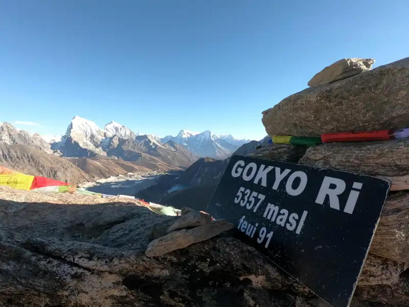 Schild auf dem Gokyo Ri Gipfel (5357 m) mit Blick auf die umliegenden Berge und den Gokyo See.