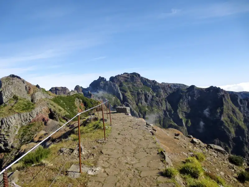 Gepflasterter Bergwanderweg mit Geländer und Blick auf die umliegende Berglandschaft.