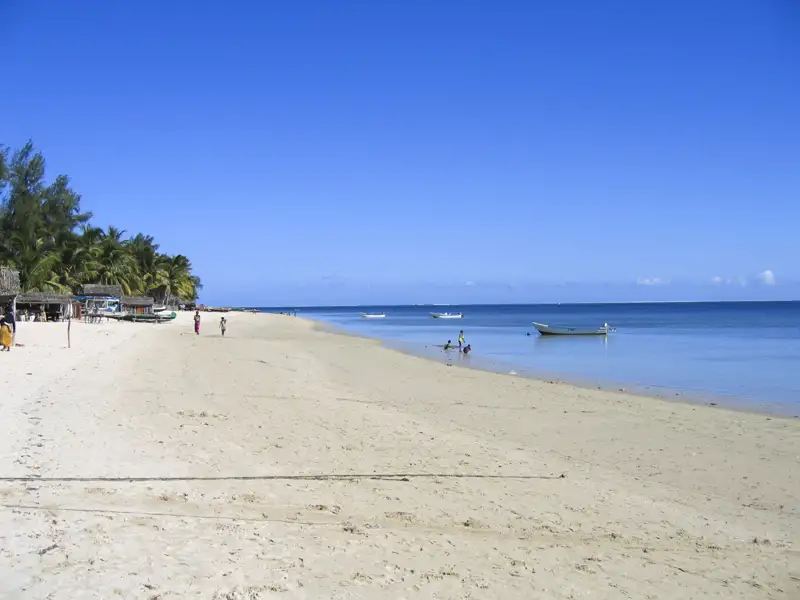 Weißer Sandstrand mit Palmen und Booten.