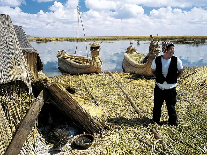 Traditionelle Schilfboote und -hütten der Uros auf dem Titicacasee. Ein Bewohner steht auf einer der schwimmenden Inseln.
