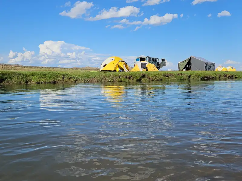 Campingplatz mit Zelten und Fahrzeug am Flussufer.