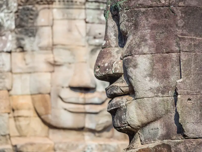 Detailansicht eines Steingesichts, das die Verwitterung durch die Zeit zeigt, mit einem weiteren monumentalen Gesicht im Hintergrund.