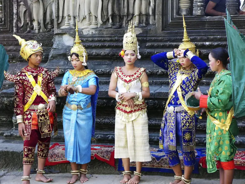 Kambodschanische Tänzer in traditionellen Kostümen posieren vor einer Tempelanlage.