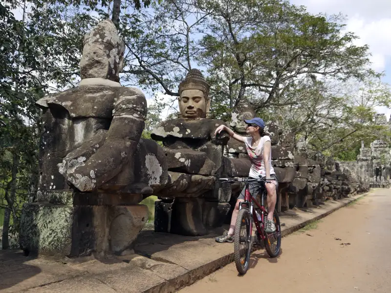 Reisende mit Fahrrad an den Steinfiguren von Angkor Thom.