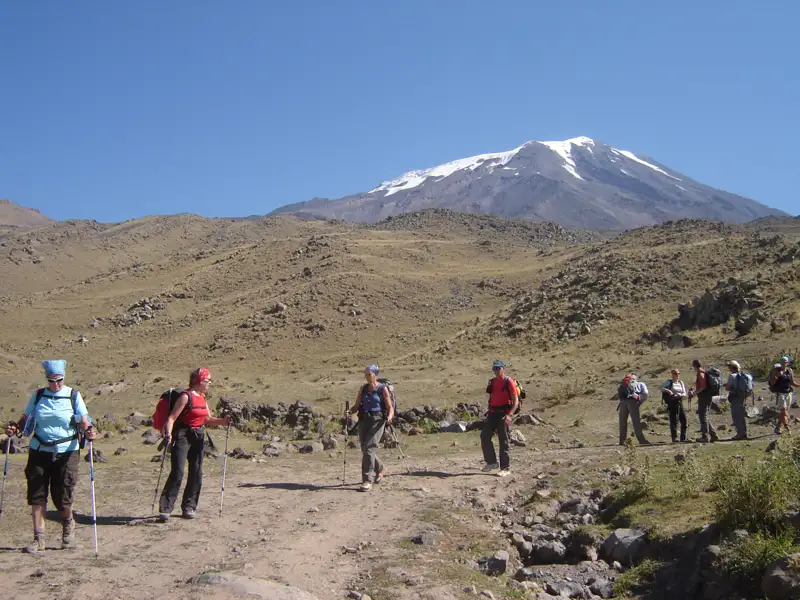 Wandergruppe auf einem Bergpfad in Richtung eines schneebedeckten Berggipfels.