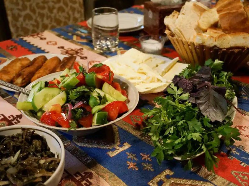Tisch mit verschiedenen traditionellen Gerichten, wie Salat, Käse, Kräutern und gebratenem Gebäck.