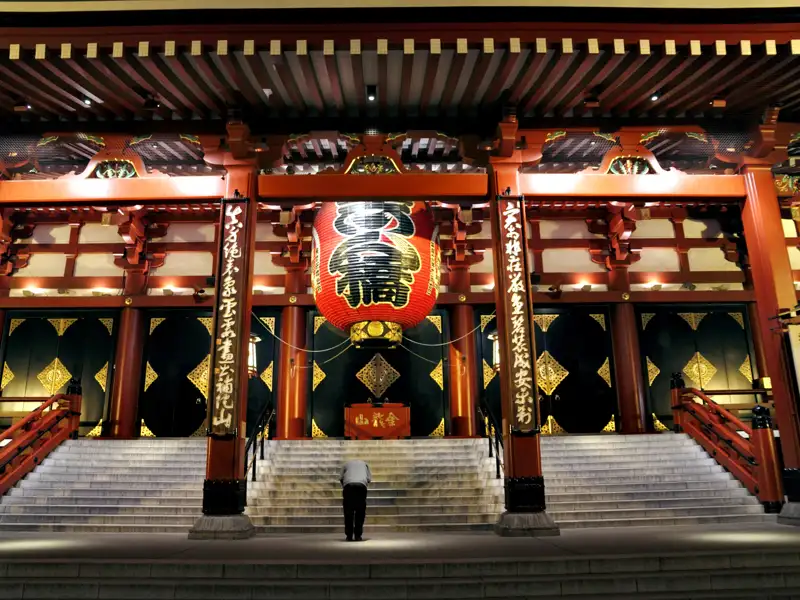 Traditioneller japanischer Tempel mit großer roter Laterne und einer Person, die sich verbeugt.