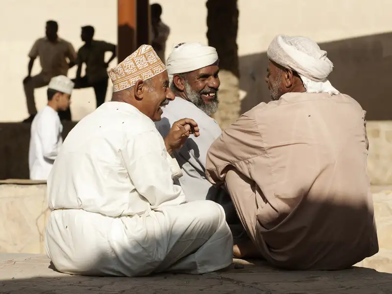 Drei Männer in traditioneller omanischer Kleidung unterhalten sich.