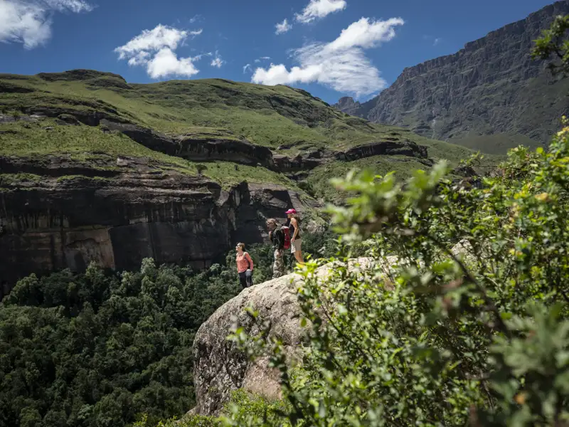 Wanderer auf einem Felsvorsprung mit Blick auf eine Berglandschaft.