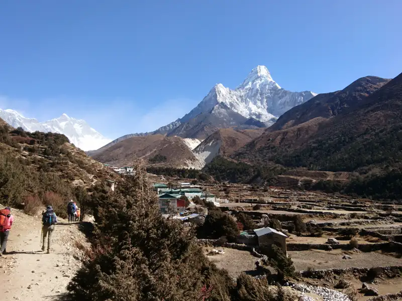 Wanderer auf einem Bergpfad in Richtung eines Dorfes mit Blick auf die schneebedeckten Berge.