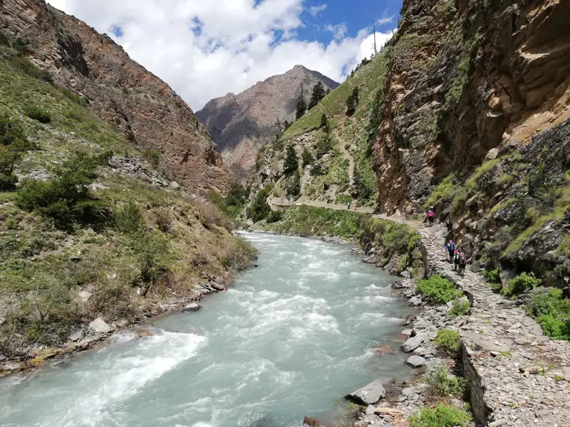 Wanderweg entlang eines Flusses in einem Gebirgstal.