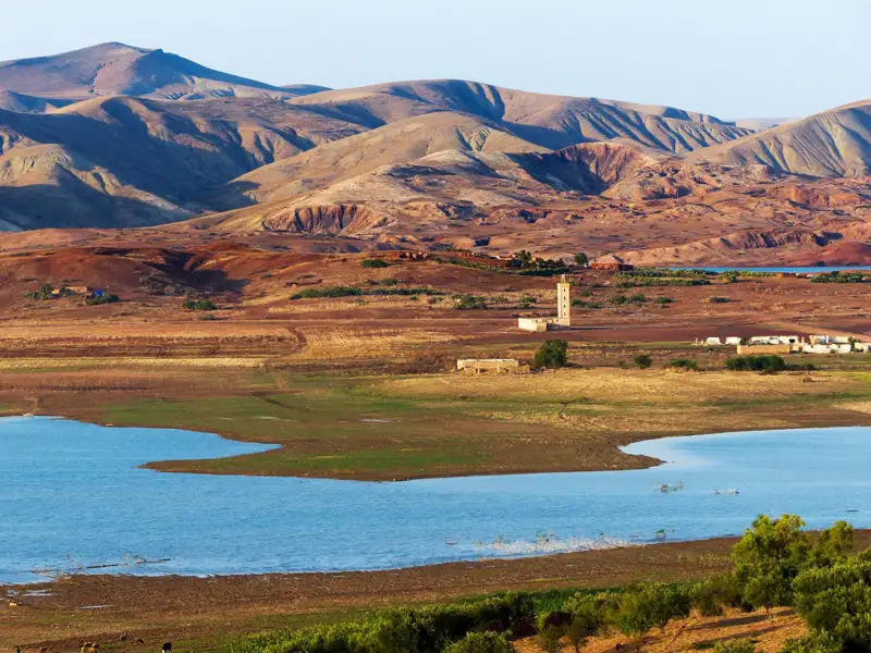 Landschaft mit See, Minarett und Bergen.