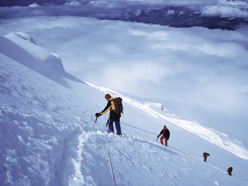Bergsteiger beim Aufstieg eines verschneiten Berges, gesichert durch ein Seil.