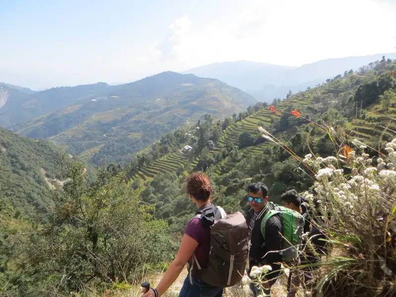 Wanderer mit Rucksäcken auf einem Bergpfad. Im Hintergrund terrassierte Reisfelder und bewaldete Hügel.