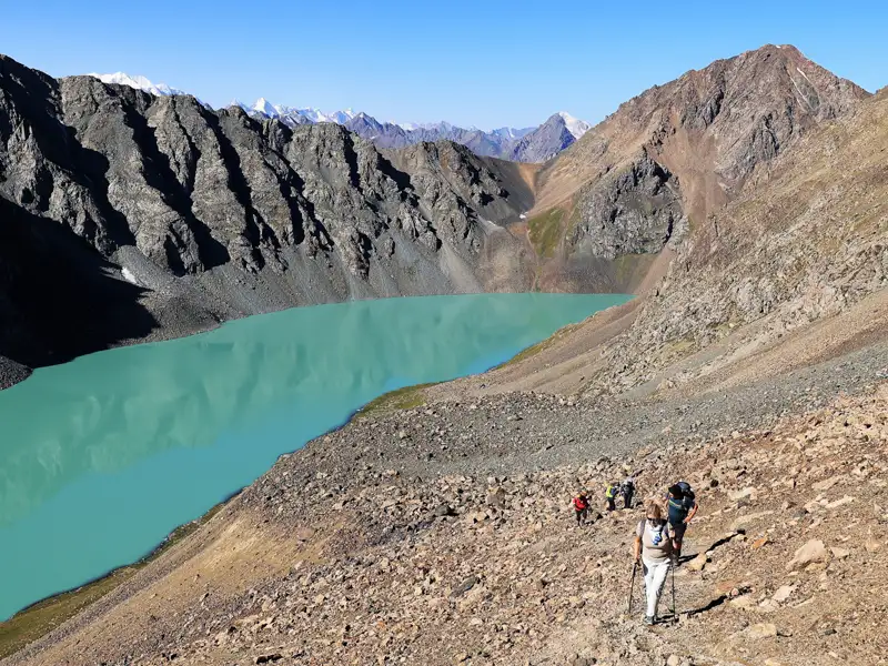 Wanderer auf einem Bergpfad in der Nähe eines türkisfarbenen Sees.