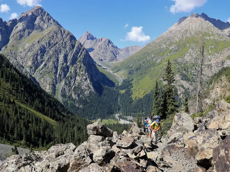 Wanderer auf einem Bergpfad mit Blick auf ein bewaldetes Tal und hohe Gipfel.