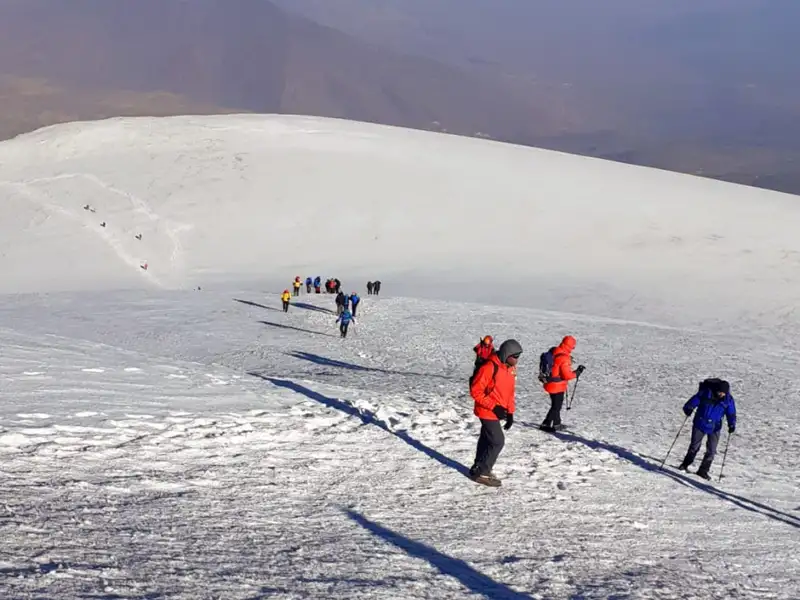 Wanderer mit Winterausrüstung besteigen einen verschneiten Berghang.