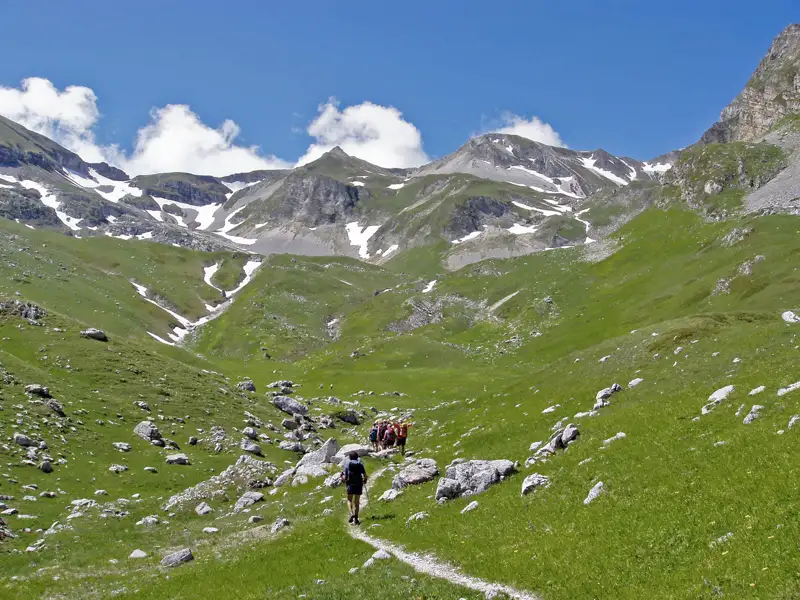Wanderer auf einem Bergpfad mit schneebedeckten Gipfeln im Hintergrund.