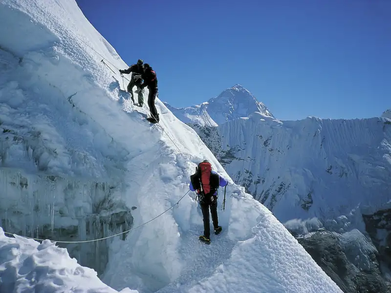 Zwei Bergsteiger mit Seilsicherung beim Aufstieg eines schneebedeckten Grats in den Bergen.