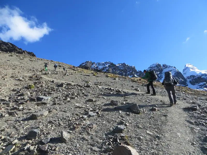 Wanderer auf einem steinigen Pfad in den Bergen. Schneebedeckte Gipfel im Hintergrund.
