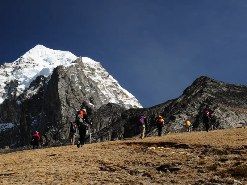 Wanderer auf einem Bergpfad in Richtung eines schneebedeckten Gipfels.