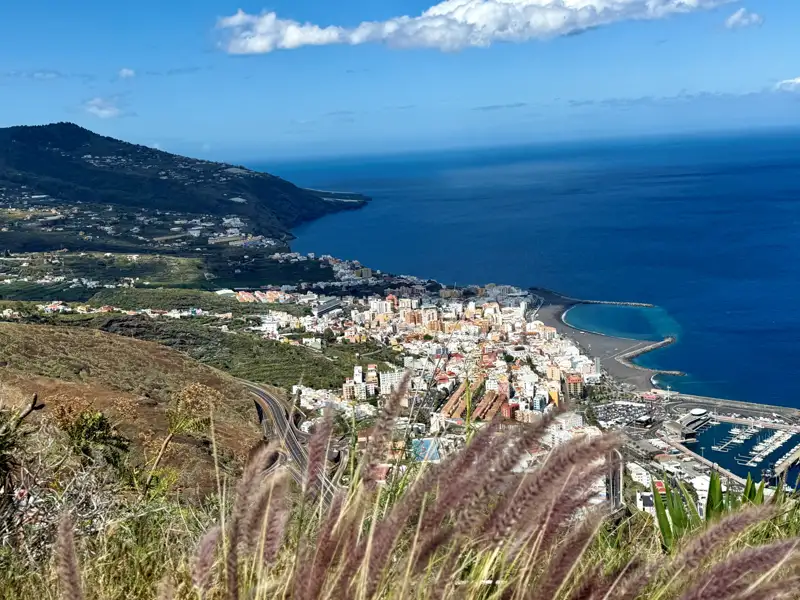 Blick über eine Küstenstadt am Meer mit Hafen und umgebender Berglandschaft.
